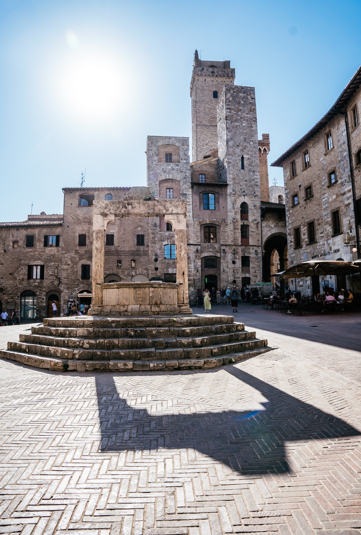 Medieval town square of San Gimignano with a large stone well in the center.