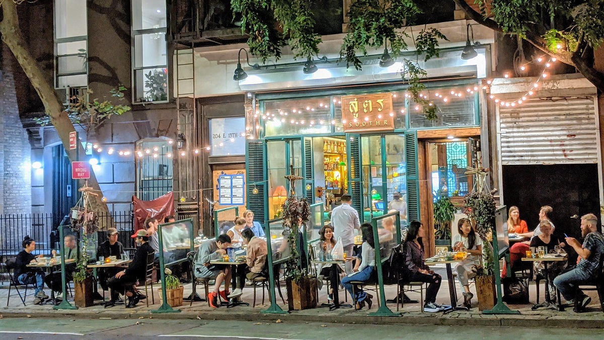 Customers eat outside at tables by a restaurante in New York City with lights