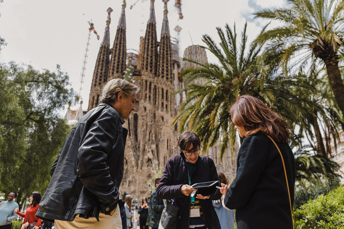 Walks guide using a tablet to show tour guests info about the Sagrada Familia with the basilica in the background