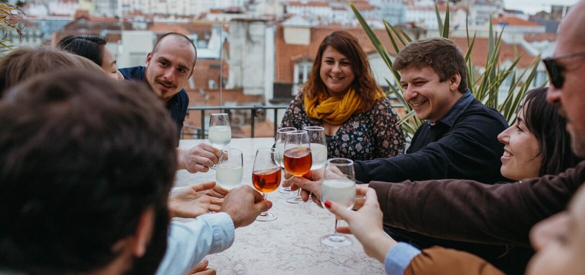 Group of people sitting outside in Lisbon raising a small glass of bright orange wine or port
