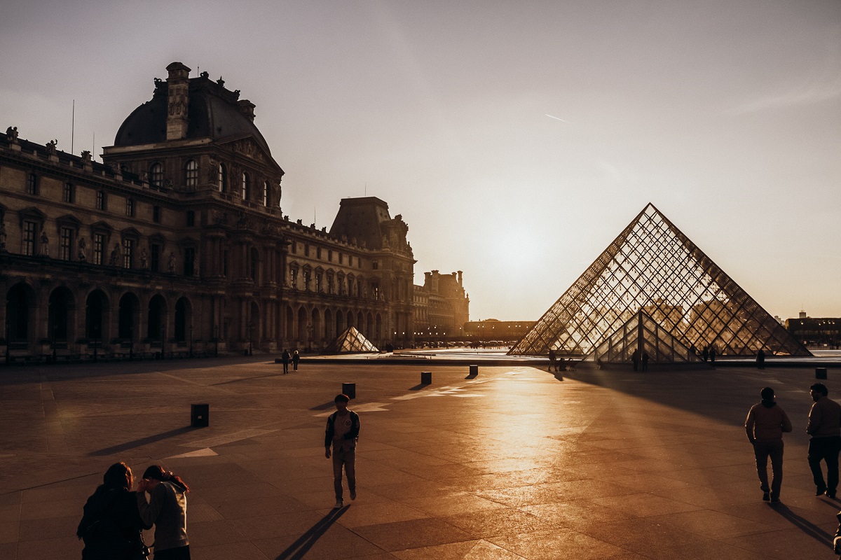 Lourve museum in Paris at sunset with people walking towards the pyramid