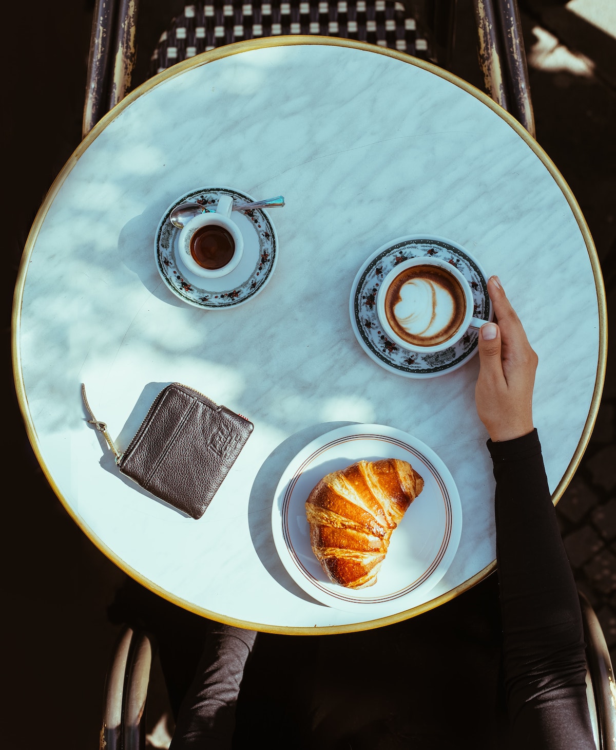 Flatlay of a cafe table in Naples. on top of the table is a cappuccino, an espresso, a plate with a croissant, and someone's wallet.