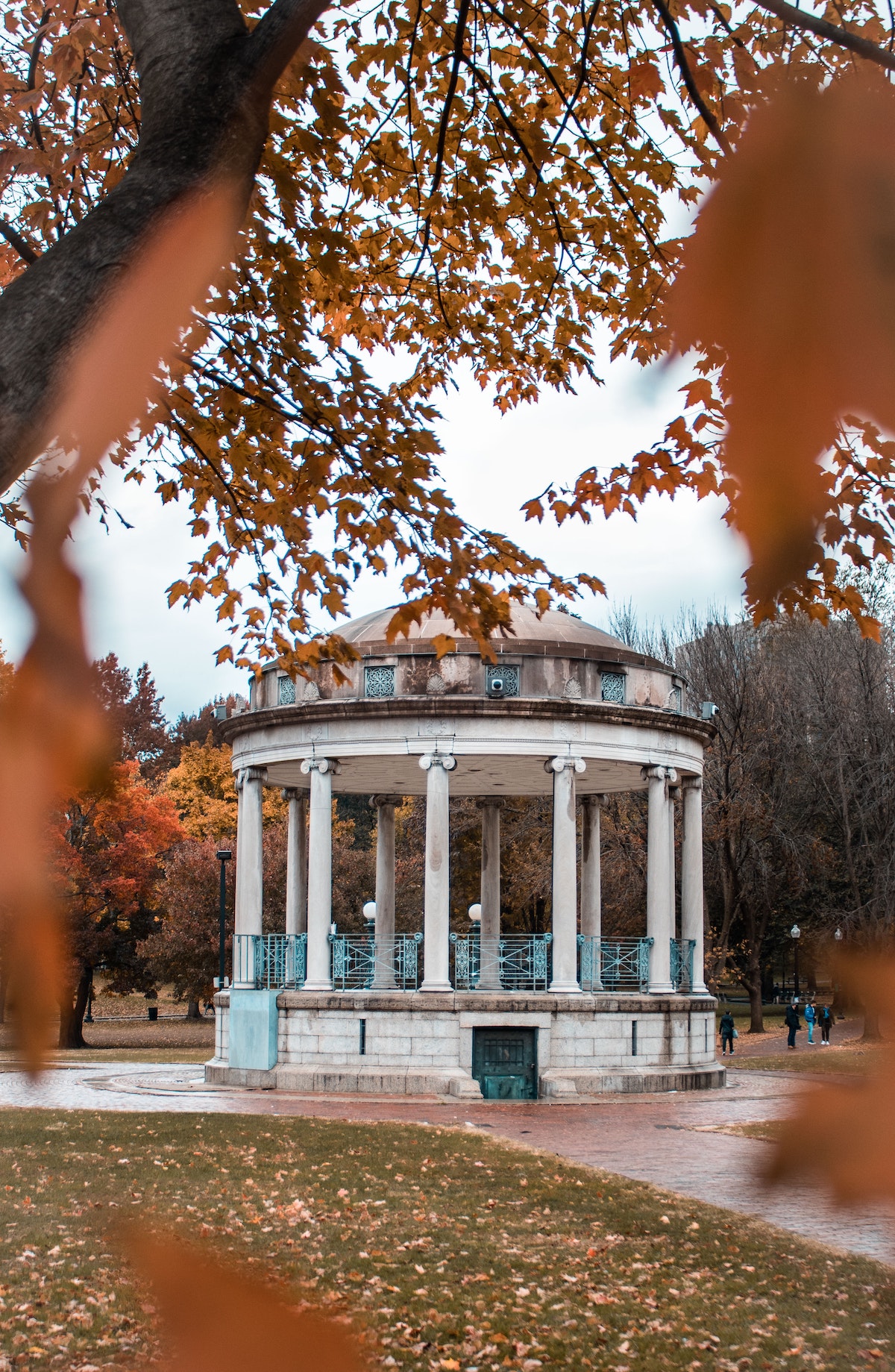 A white and blue gazebo hides behind a frame of orange leaves in the Boston Common
