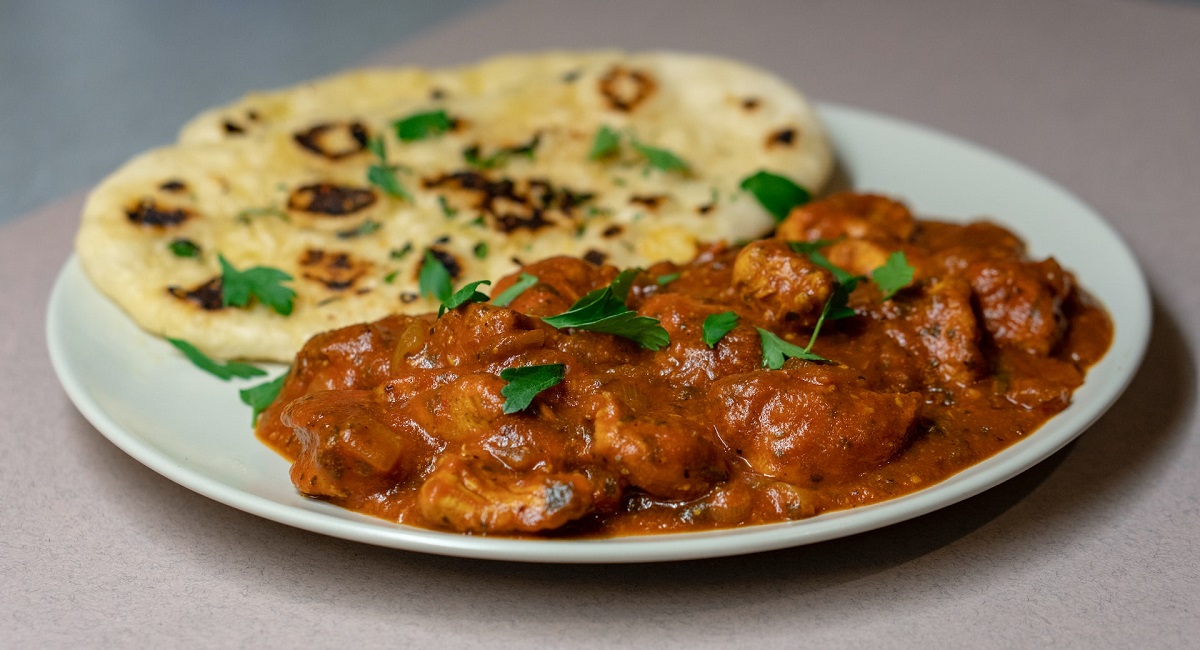 A plate with stewed chicken in a red sauce with naan