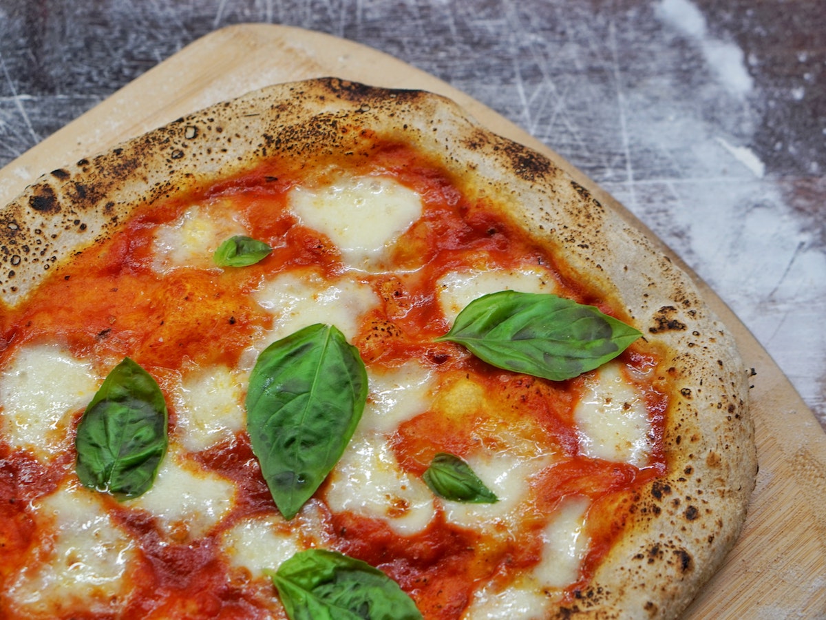close up of a pizza margherita, light brown crust with tomato sauce, melty mozzarella, and topped with fresh basil leaves