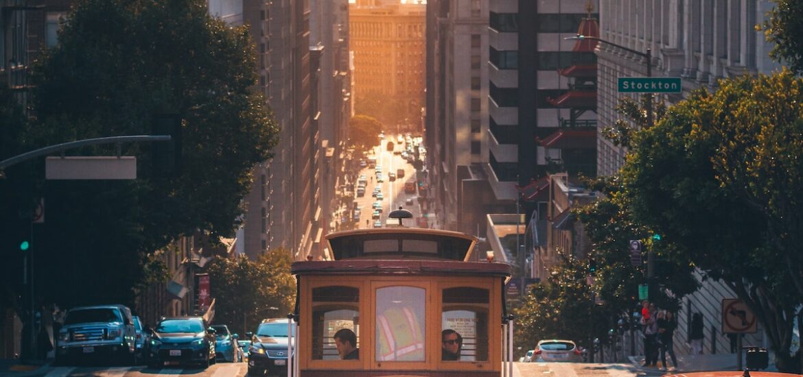 A view of cable car on a sloping street in San Francisco with a bridge in the background peeking in between buildings
