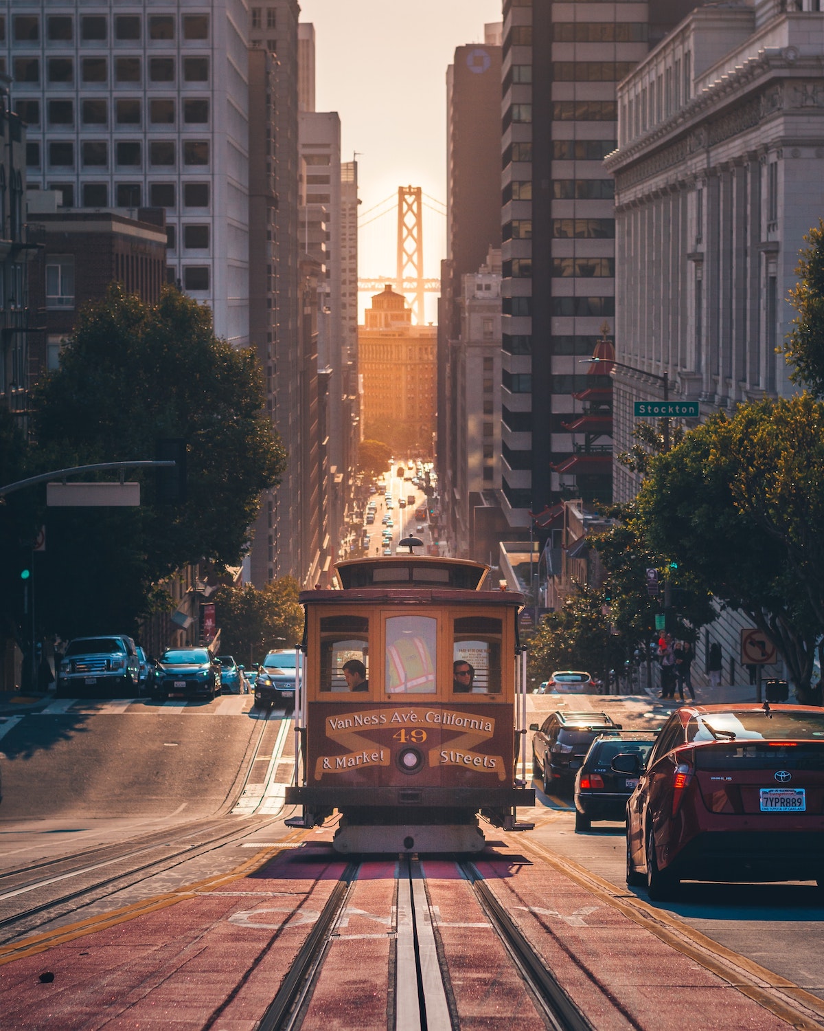 A view of cable car on a sloping street in San Francisco with a bridge in the background peeking in between buildings 