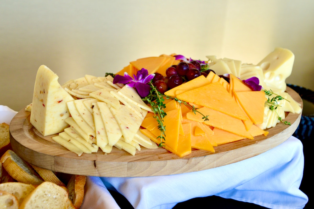 An assortment of cheese garnished with edible flowers and herbs atop a wooden board