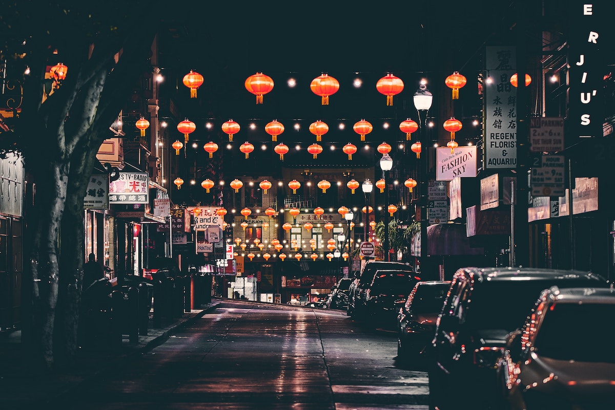 A shot of a dark street in San Francisco's Chinatown at night, with red paper lanterns strung up and lighthing the way