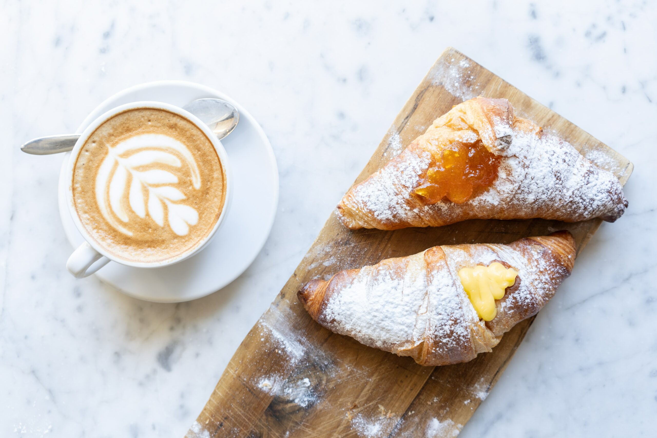 Wooden plate with two Italian cornetti pastries and a cappucino