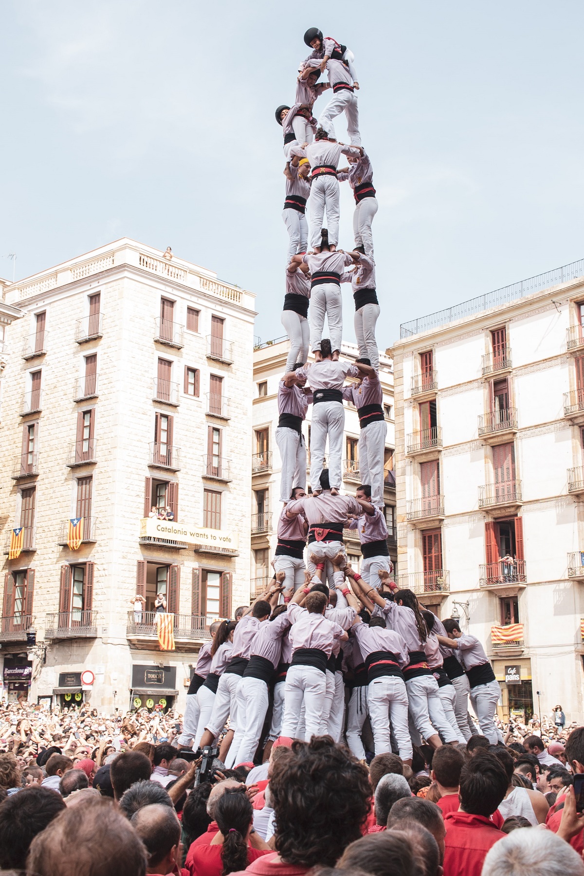 Human pyramid with castellers wearing white outfits and black belts with city in background