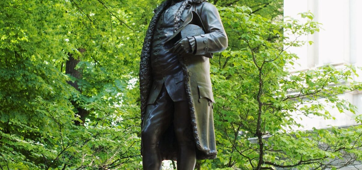 Bronze statue of Benjamin Franklin surrounded by bright freen foliage