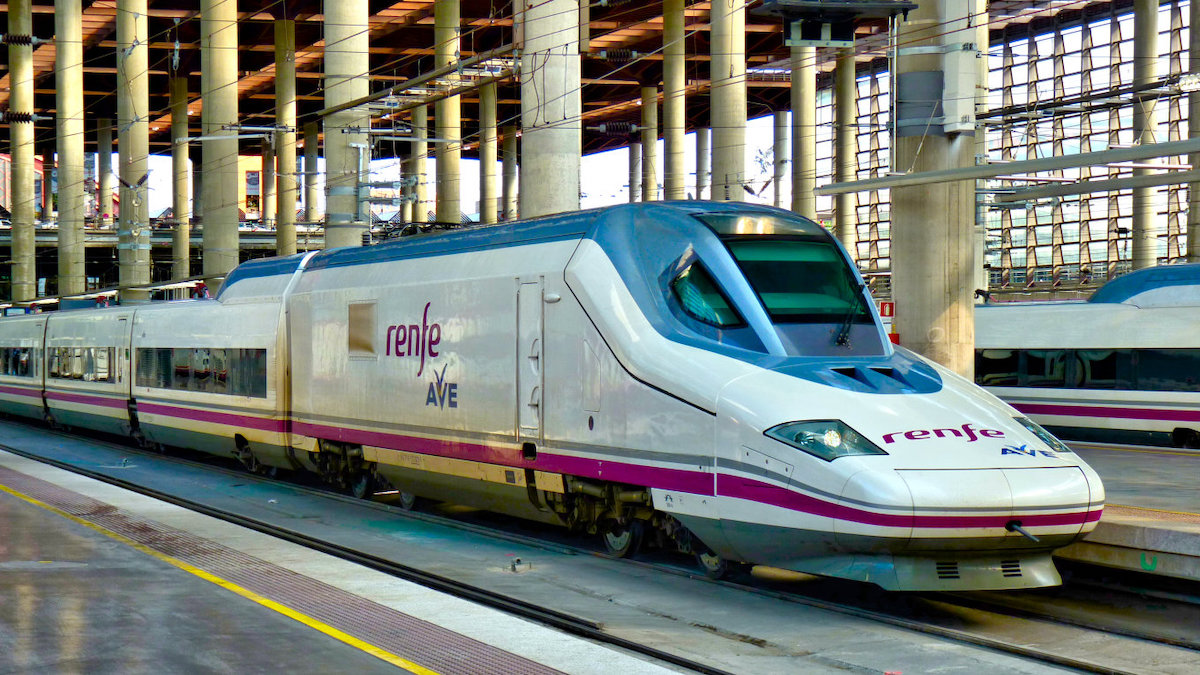 White and purple high-speed train reading Renfe AVE waiting at Madrid's Atocha station.