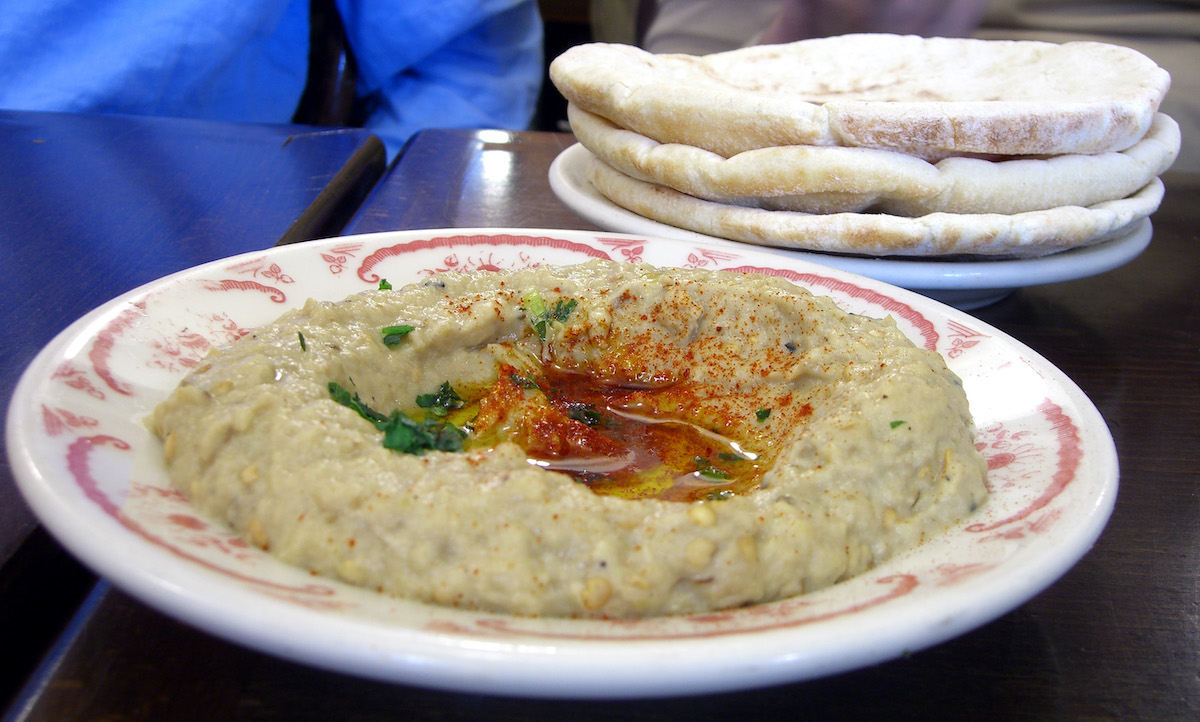 Baba ghanoush served on a red and white ceramic plate with a stack of pitas in the background.
