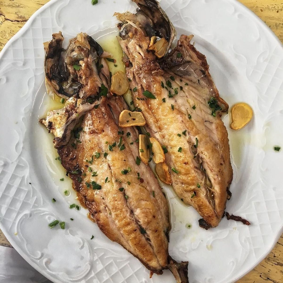 Two pieces of cooked fish garnished with herbs on a white plate.