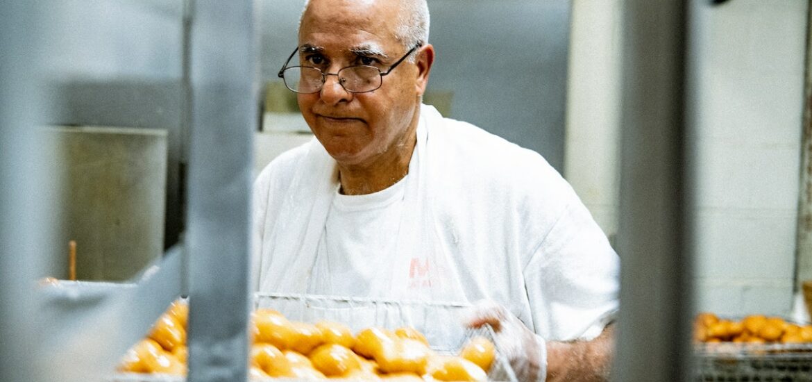 A man wearing a white shirt and glasses holding a wire basket of baked goods
