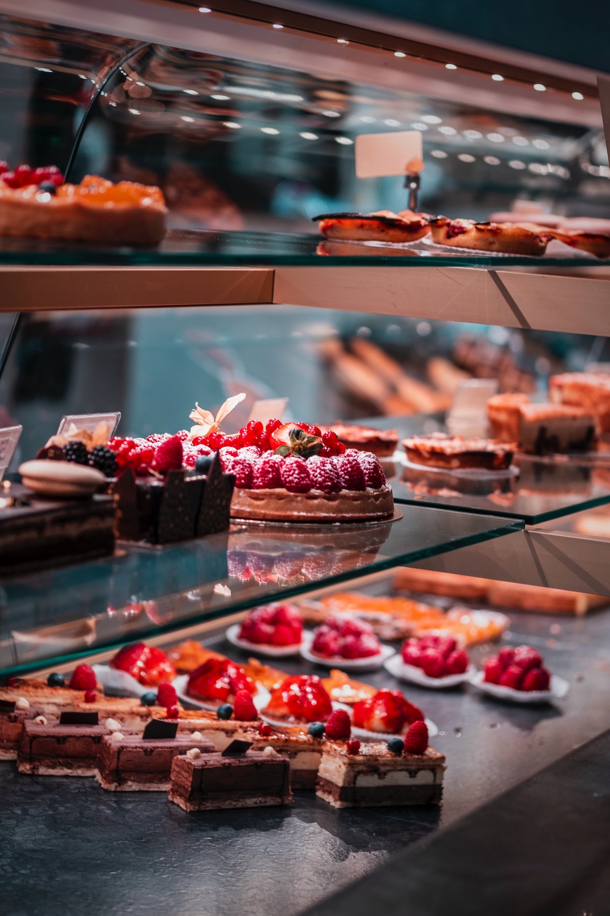 Small cakes garnished with strawberries and other fruits in a bakery display case.