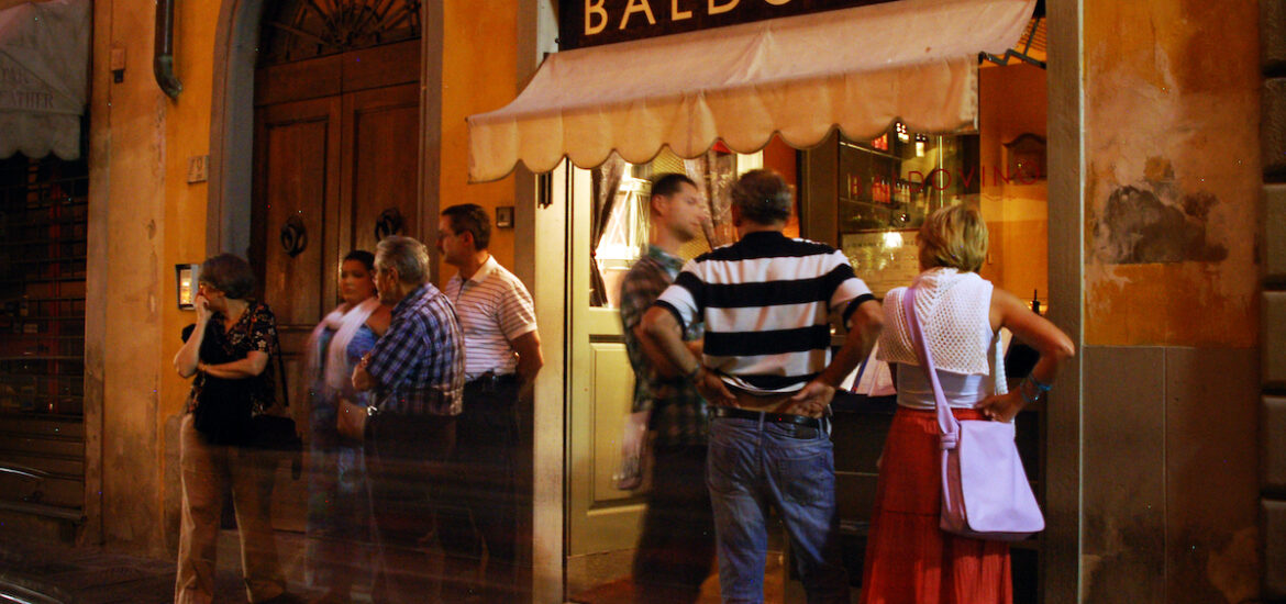 Groups of people standing outside a restaurant with the name Baldovino above an awning.