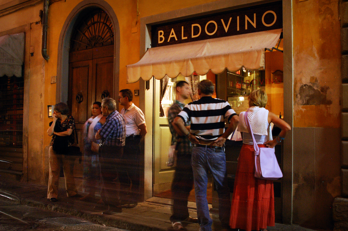 Groups of people standing outside a restaurant with the name Baldovino above an awning.