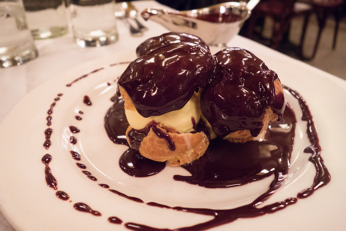 Profiteroles covered in chocolate sauce on a white plate