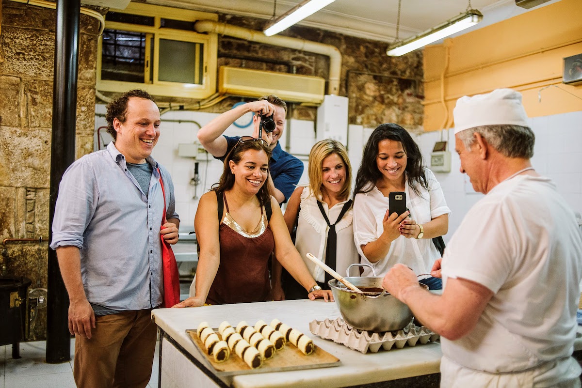 A group of people watching a baker dip pastries into chocolate.