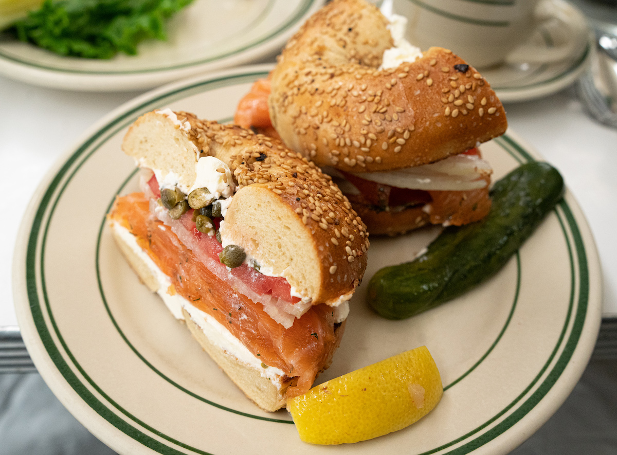 Cream cheese and lox bagel on a plate beside a pickle and a lemon slice