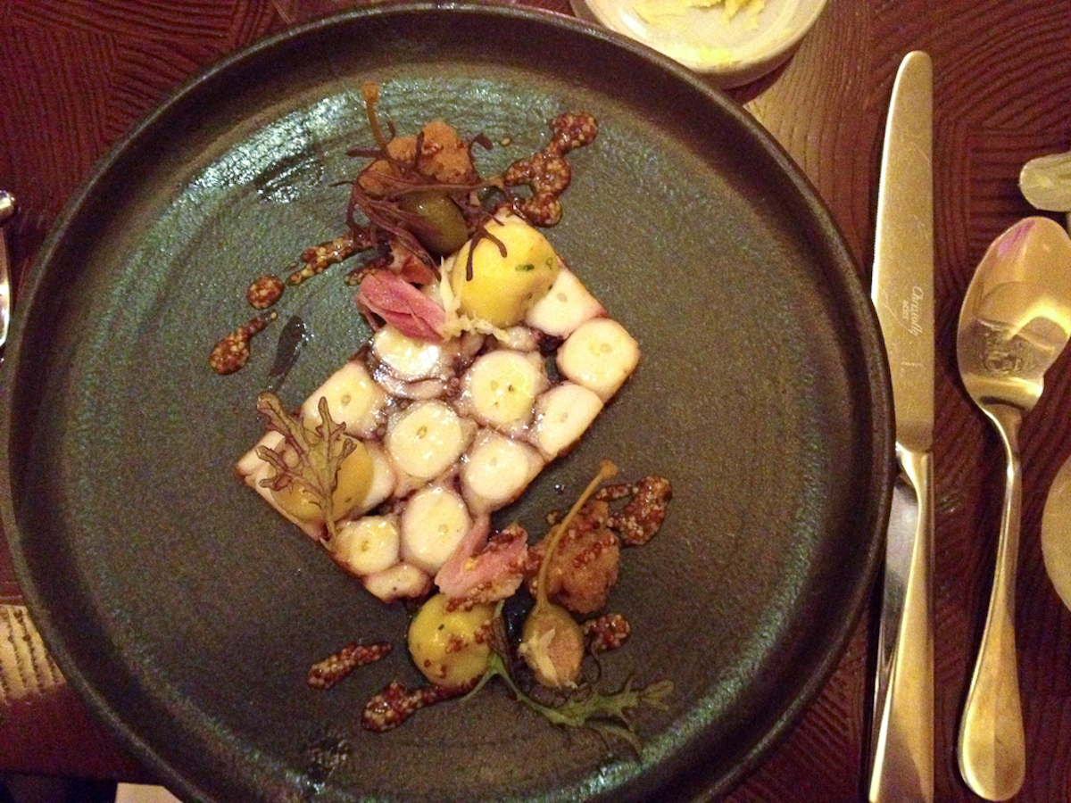 Modern presentation of octopus and potato dish on a black plate