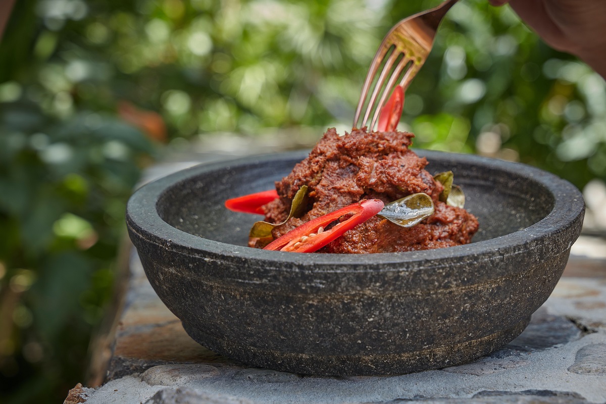 Fork diving into a dark black dish of Indonesian beef rendang