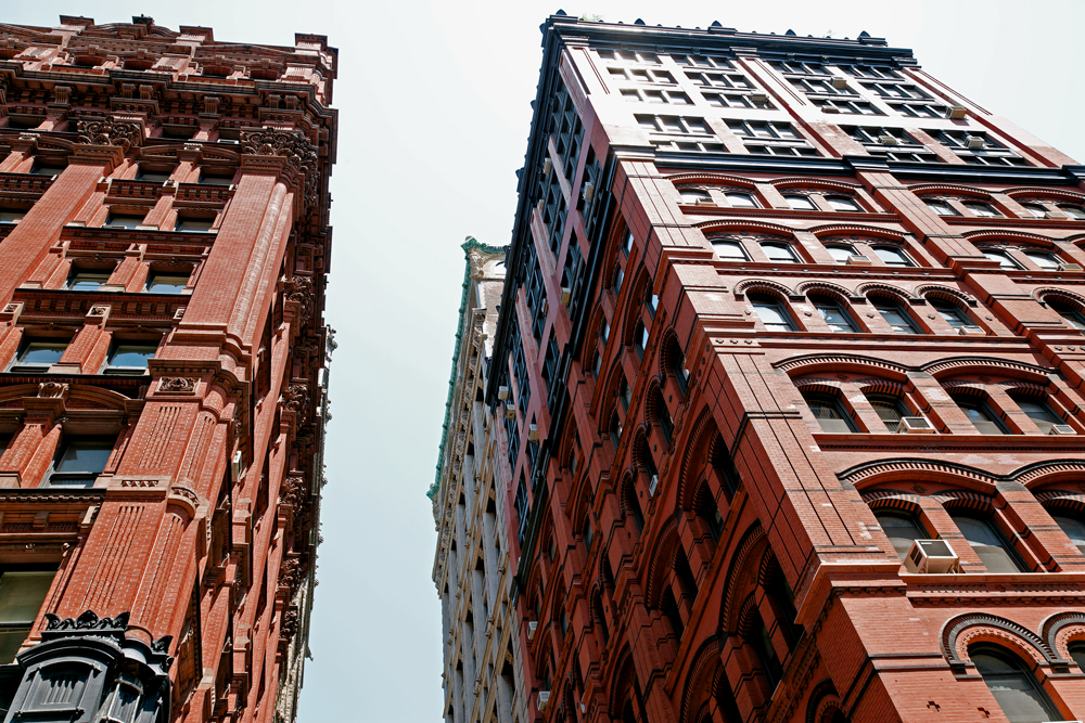 Two tall brick buildings against the sky as seen from below