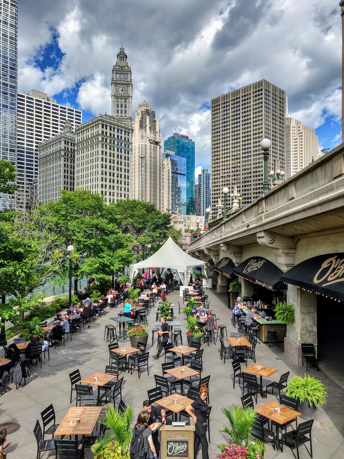 A view of Chicago loop with a restaurant with outdoor seating in the bottom foreground and the city skyline in the background. There are over 7,000 places to eat in Chicago.