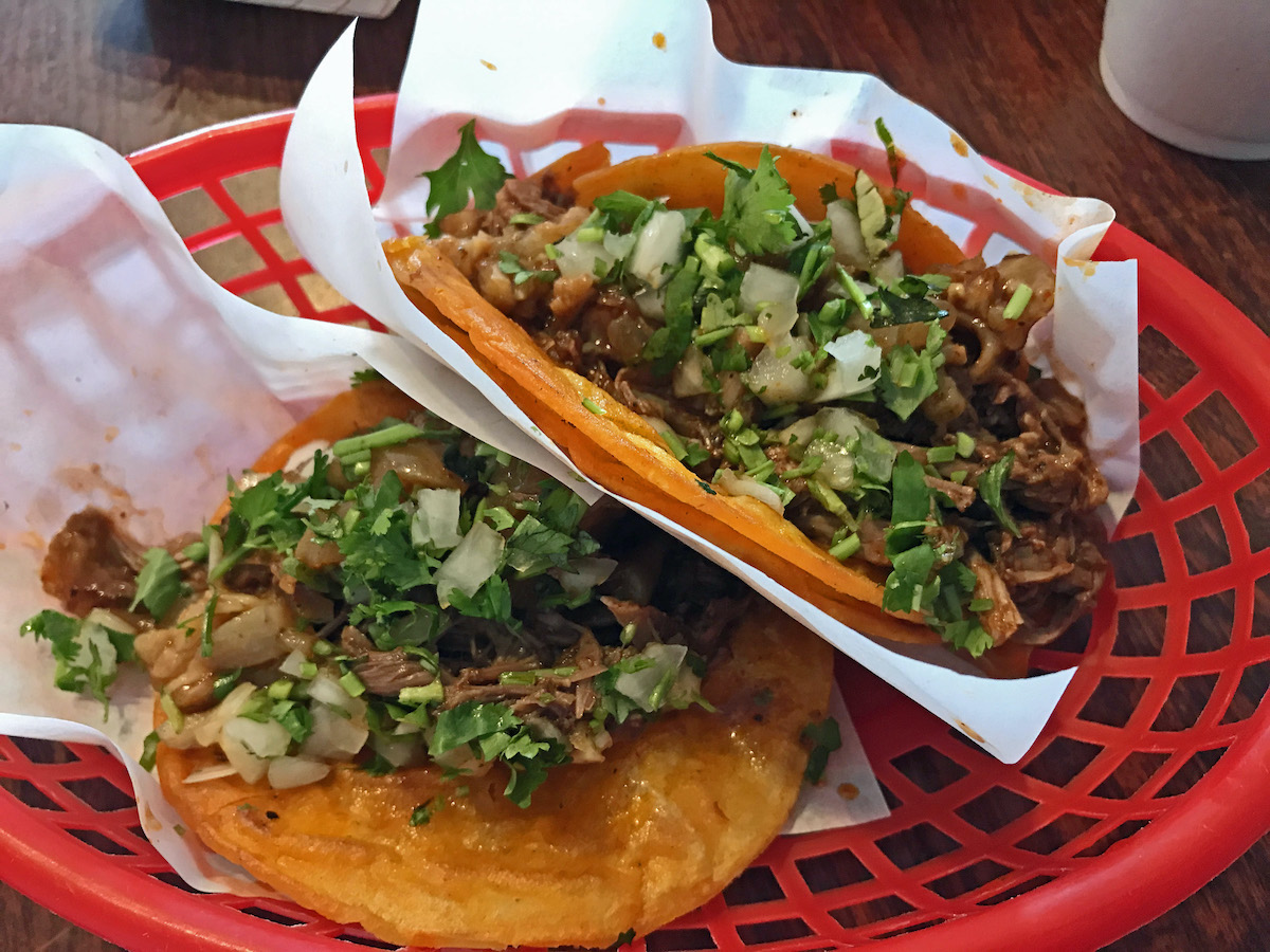 Two small tacos of beef, cilantro, and onion served in a red basket