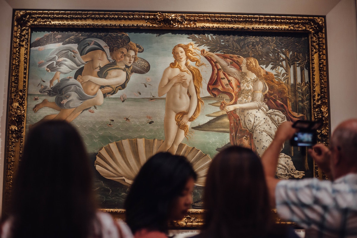 A group of people standing in front of the Birth of Venus painting at the Uffizi Museum in Florence
