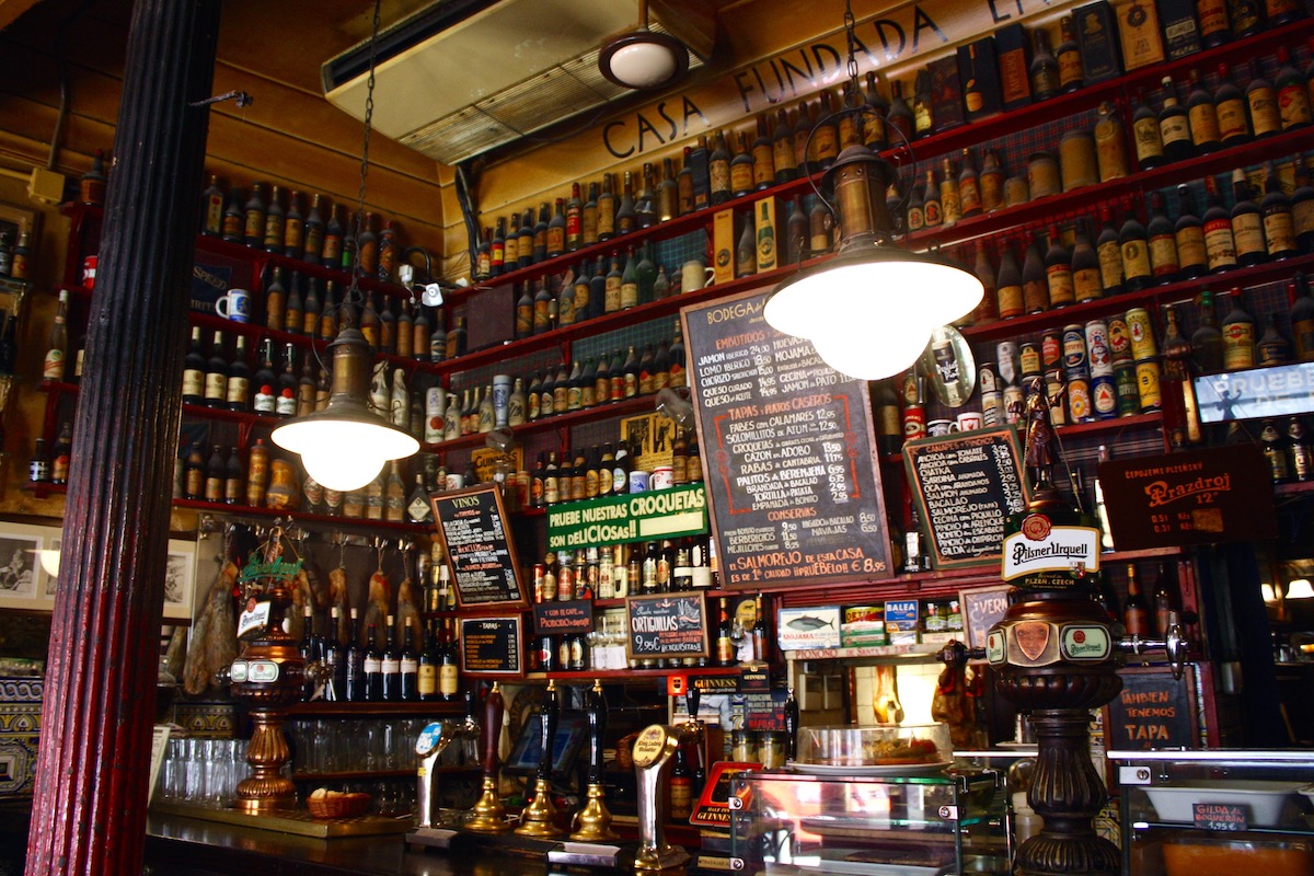 Interior of an old-fashioned Spanish bar with dark wood paneling and many shelves full of liquor bottles