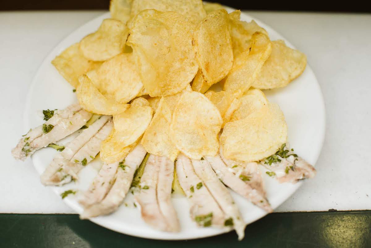 Overhead shot of anchovies marinated in vinegar in front of a pile of potato chips on a white plate