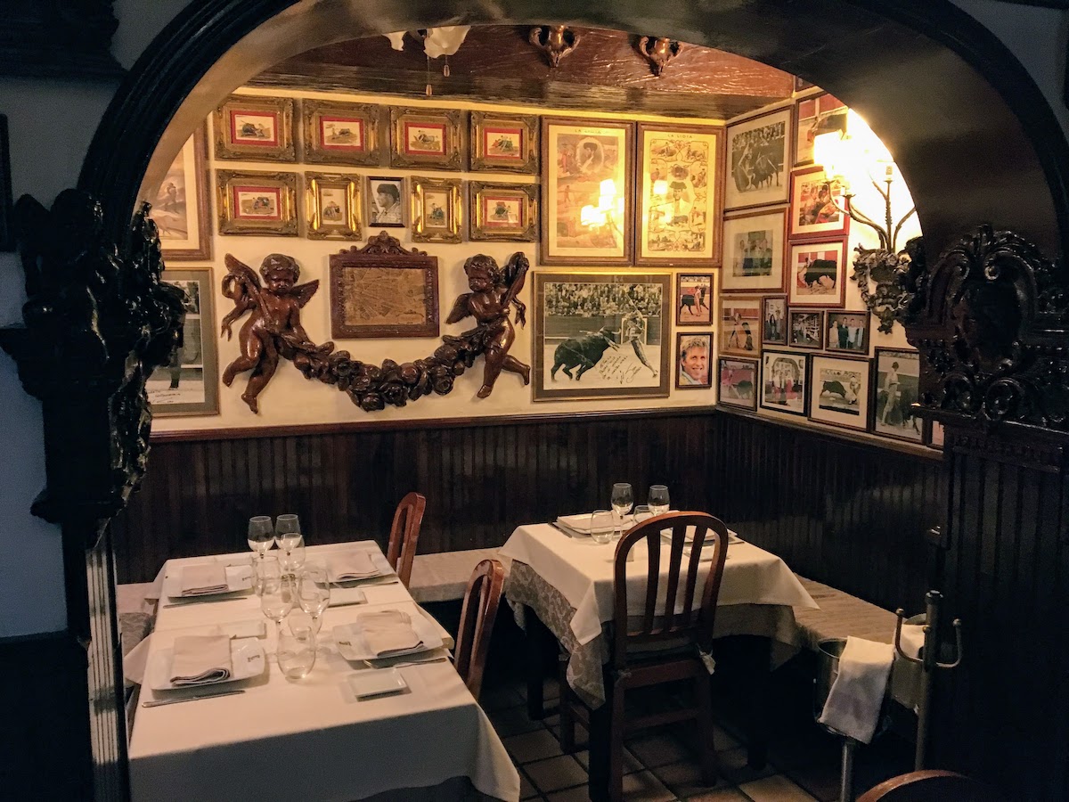 Restaurant interior with dark wood paneling, photos and decorations on the walls, and tables set with white tablecloths.