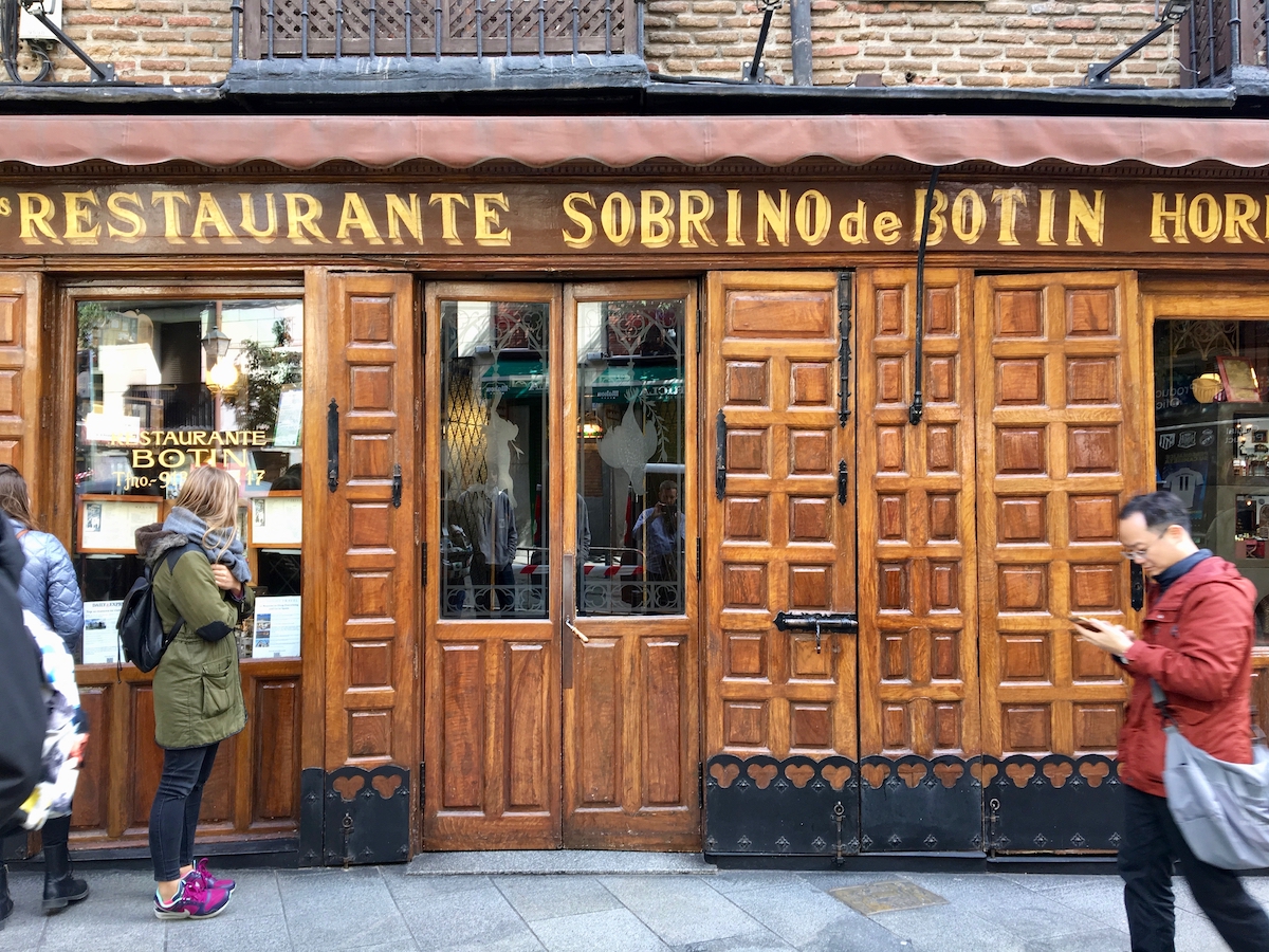Wood-paneled front entrance of Botin restaurant in Madrid, with a sign under a small brown awning reading Restaurante Sobrino de Botin.