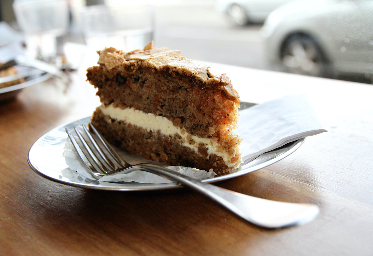Slice of carrot cake with cream cheese frosting dividing the layers on a plate beside a fork.