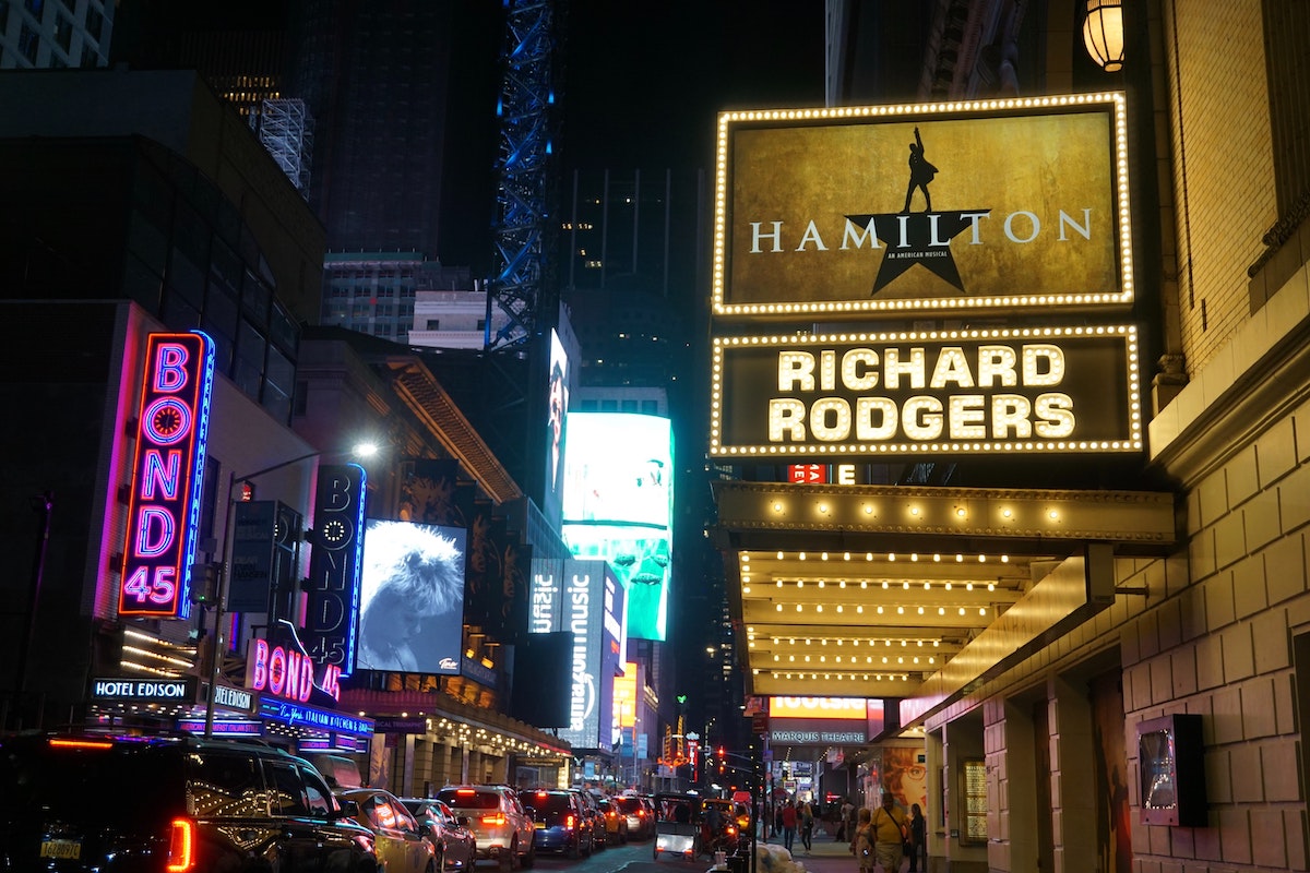View looking down Broadway in NYC at night, with a marquee for Hamilton in the foreground