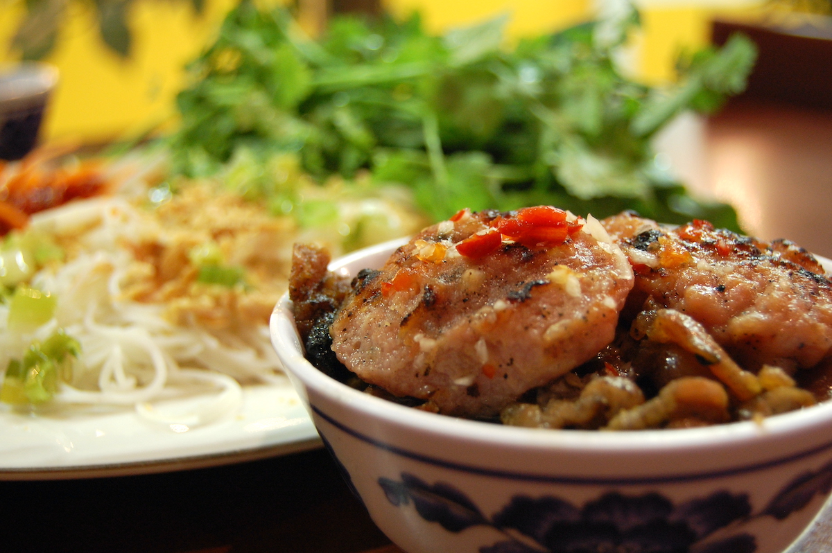Vietnamese pork sausage in a ceramic bowl with a plate of vermicelli noodles in the background.