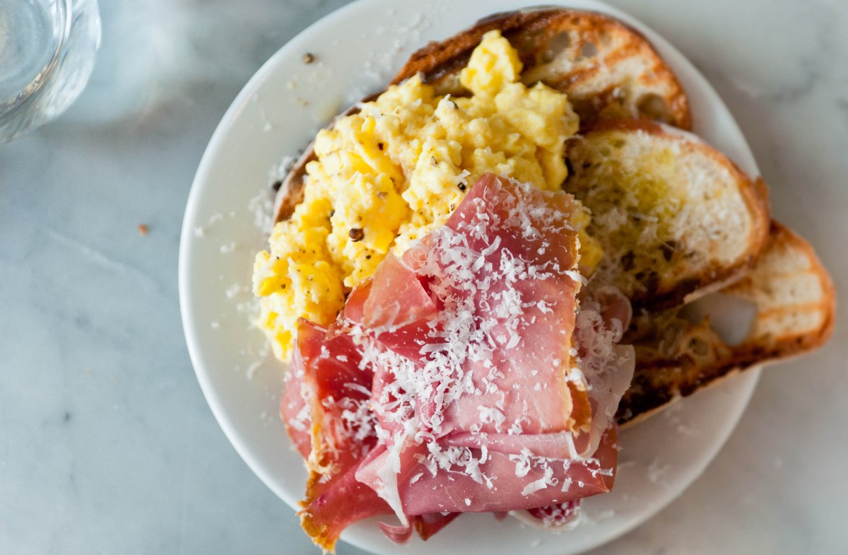 Overhead shot of cured meats, scrambled eggs, and toast on a white plate