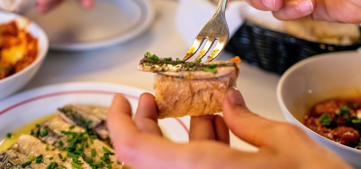 Close up of a person putting a small piece of fish atop a chunk of bread with a fork
