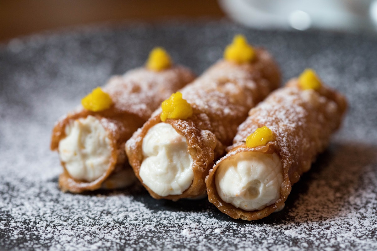 Three cannoli on a plate dusted with powdered sugar