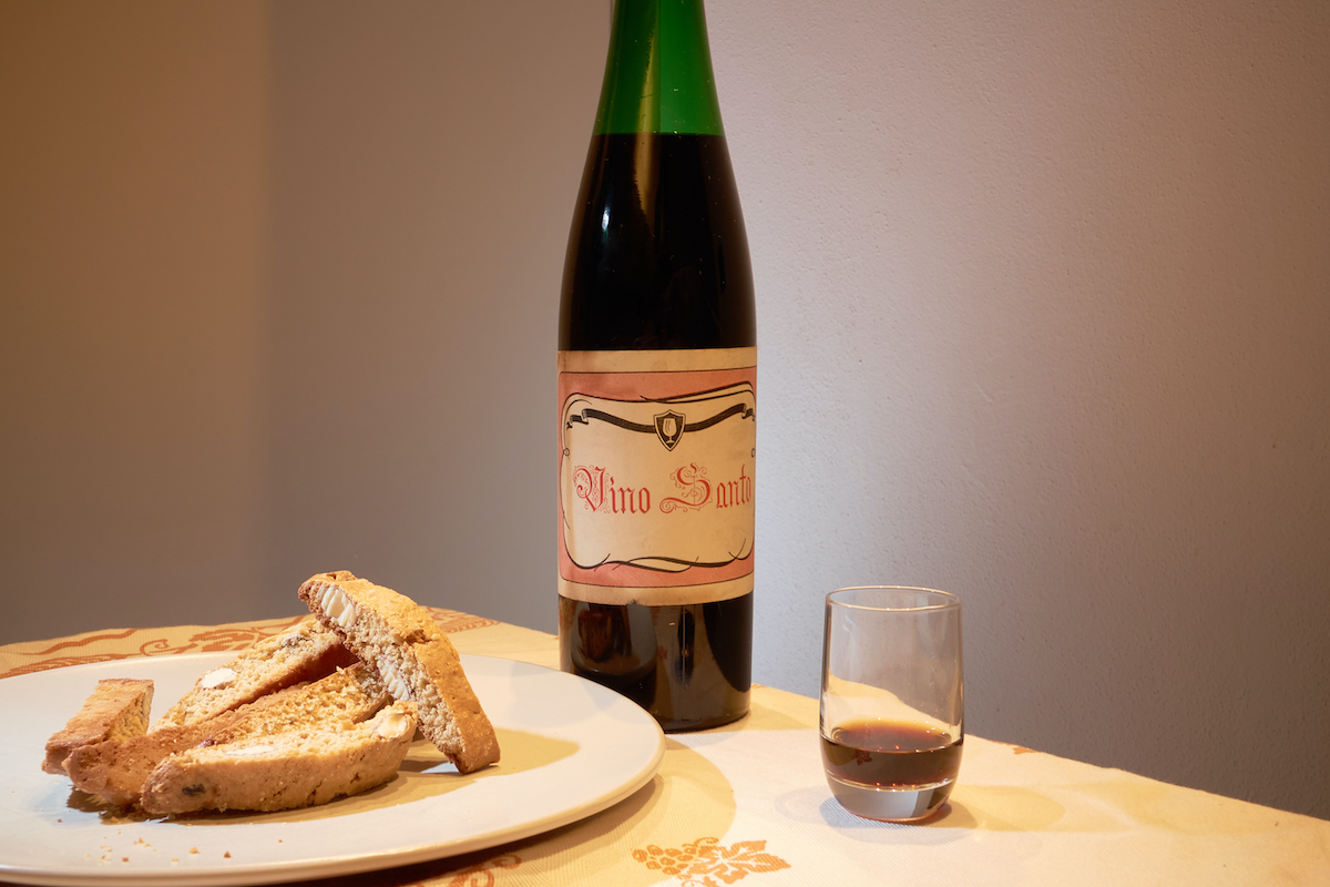 Plate of biscotti-like cookies on a table beside a bottle and a small glass of sweet wine.