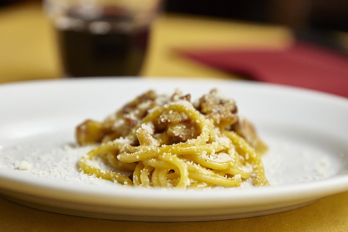 Spaghetti carbonara served on a white plate with a stemless glass of red wine in the background