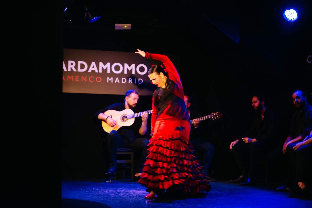 Flamenco dancer performing in a red dress, with two guitar players and two singers seated behind her.