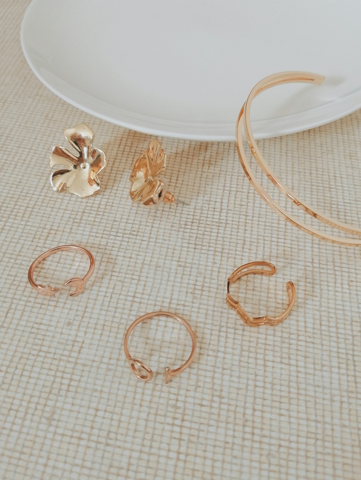 A pair of flower earrings, a bracelet, and 3 gold rings on a jewelry dish with white background