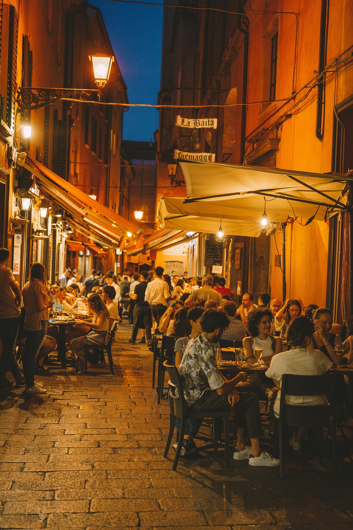 Street in Bologna filled with restaurants at night with people eating on the sidewalk