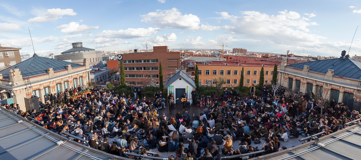 Overhead view of an audience watching a live music performance on an outdoor rooftop terrace. 