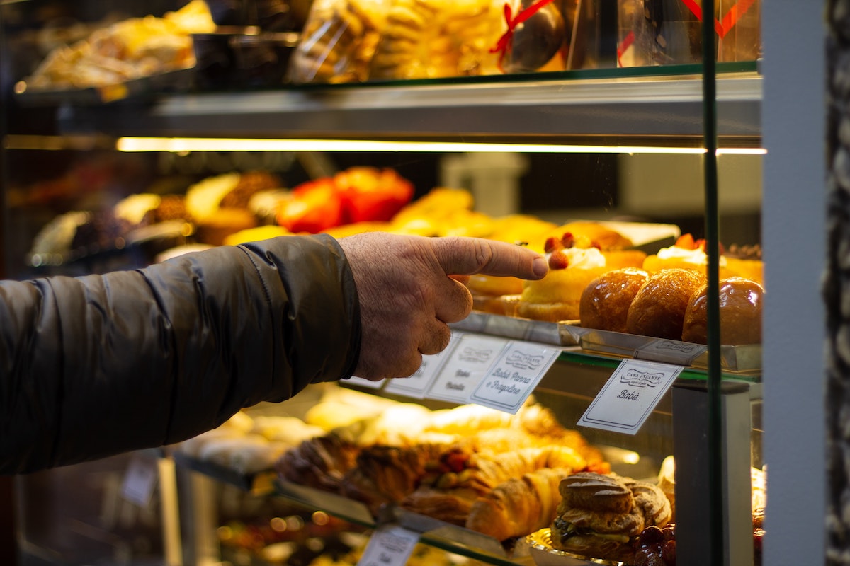 Someone points at a baba inside a pastry display case in Naples