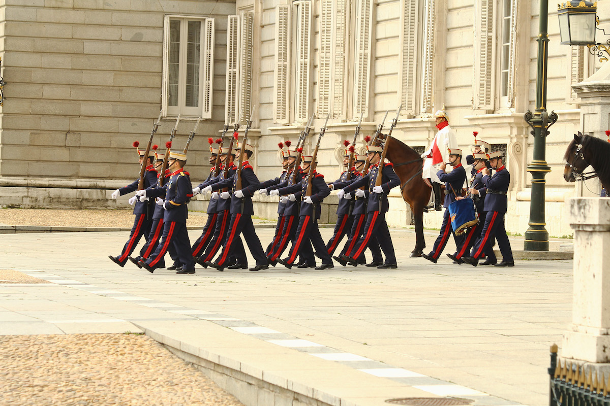 Group of military members in dress uniforms walking in unison during a formal ceremony.